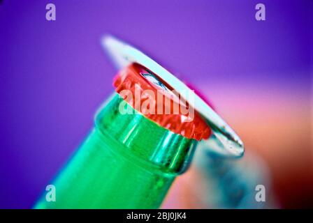 Bottle opener removing cap from bottle of beer - Stock Photo