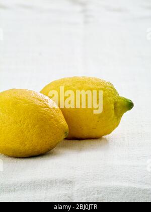Two whole lemons on white linen cloth background - Stock Photo