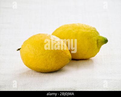 Two whole lemons on white linen cloth background - Stock Photo