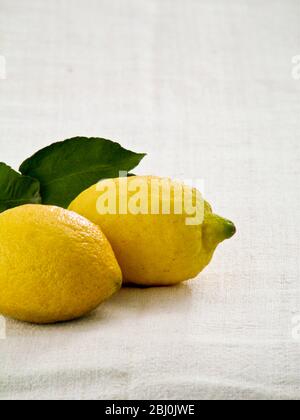Two whole lemons with leaves on white linen cloth background - Stock Photo