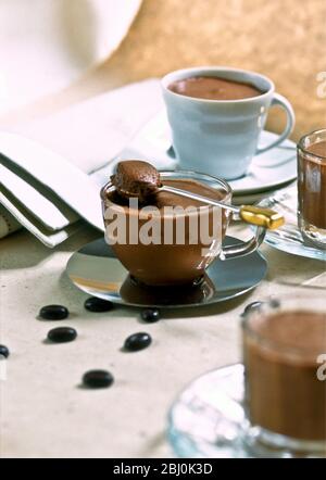 Chocolate mousse served in a variety of pretty cups with coffee bean chocolates scattered around on table - Stock Photo