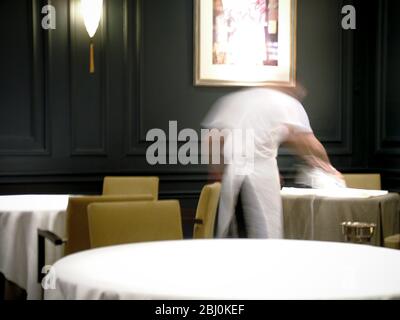 Pressing white linen table cloth in dark restaurant interior before service - Stock Photo