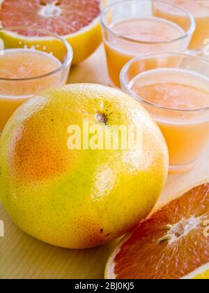 Little glasses of pink grapefruit juice with whole and halved grapefruit - Stock Photo