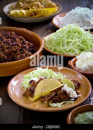 Mexican meal of tacos with chilli con carne shredded lettuce, plain rice, and sour cream - Stock Photo