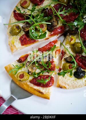 Pizza with sundries tomatoes, aubergine, olives, mozzarella and rocket - Stock Photo