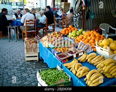 Fruit stall outside shop with men playing game and drinking coffee in the background. Dalyan, Anatlia, Turkey - Stock Photo