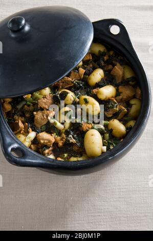 Black earthenware casserole with dish of pork spinach and potatoes with soy sauce - Stock Photo