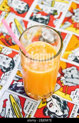 Freshly squeezed orange juice in cafe glass on table cloth with comic strip pattern - Stock Photo
