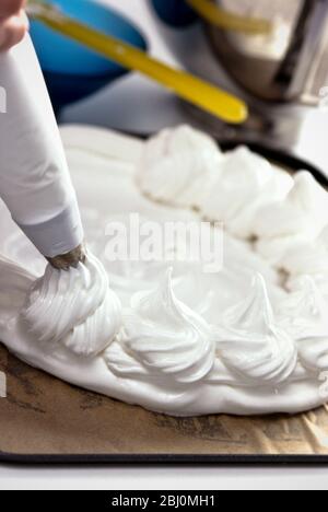 Piping meringue swirls around the edge of a meringue base to make a classic Pavlova - Stock Photo