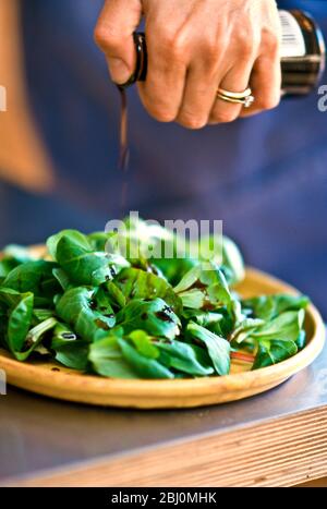 Drizzling balsamic vinegar onto lamb's lettuce in pottery dish. - Stock Photo