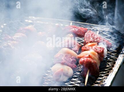 Grilling scallop and steak kebabs on a charcoal fired barbecue grill - Stock Photo