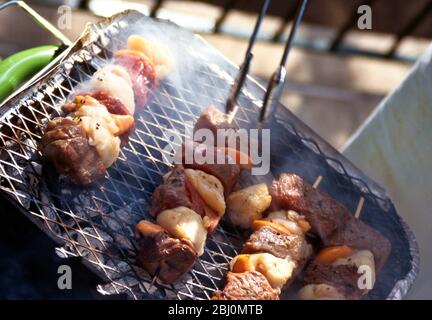 Grilling scallop and steak kebabs on a charcoal fired barbecue grill - Stock Photo