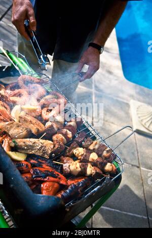 Grilling scallop and steak kebabs, red peppers, mediterranean prawns, and tuna steaks, on a charcoal fired barbecue grill - Stock Photo
