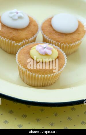 Shop bought fairy cakes on yellow enamel plate - Stock Photo