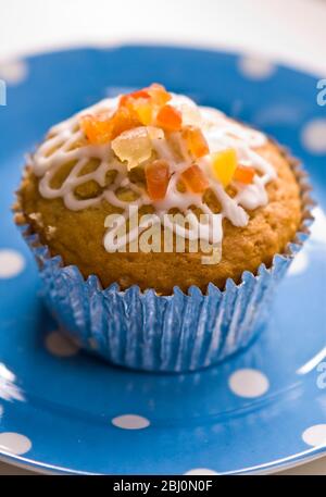Muffin decorated with squiggly icing and candied peel on spotted blue plate - Stock Photo