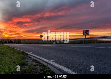 winding asphalt road against the backdrop of a dramatic, fiery sunset Stock Photo