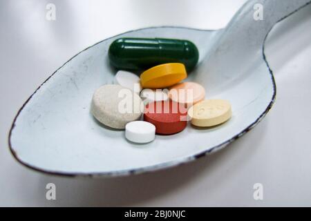 White enamel spoon of various coloured pills - Stock Photo