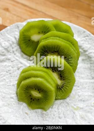 Slices of peeled kiwi fruit on white textured plate - Stock Photo