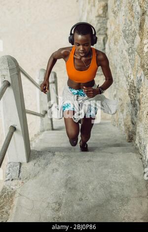 Female exercising outdoors on steps. Sports woman running up stairs wearing headphones. Stock Photo