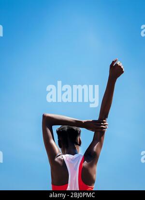 Rear view of a fitness woman stretching hands against blue sky outdoors. African female warming up before exercising outdoors. Stock Photo