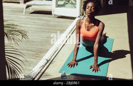 Healthy woman exercising at home on yoga mat. Fitness woman practicing yoga to stay fit. Female in cobra yoga pose at the poolside. Stock Photo