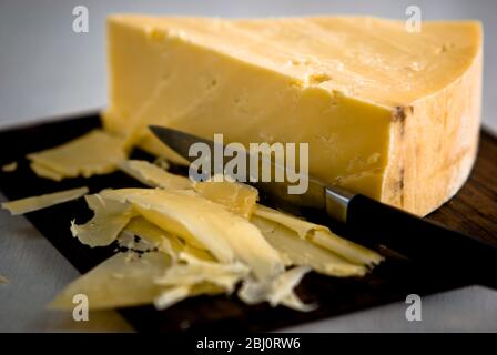 Wedge of cheddar cheese, being cut on wooden cheeseboard - Stock Photo