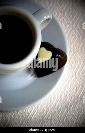 Heart shaped chocolate on saucer of small espresso cup of black coffee - Stock Photo