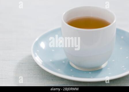 Calming cup of herb or china tea in fine porcelain cup without handle on spotted blue and white saucer - Stock Photo