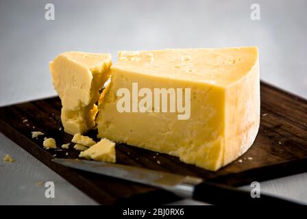 Wedge of cheddar cheese, being cut on wooden cheeseboard - Stock Photo