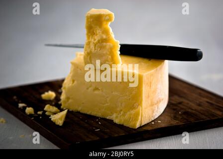 Wedge of cheddar cheese, being cut on wooden cheeseboard - Stock Photo