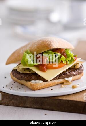 Gournet cheeseburger with salad and tomato on ciabatta bread roll on flat white porcelain plate. - Stock Photo