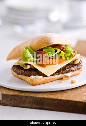 Gournet cheeseburger with salad and tomato on ciabatta bread roll on flat white porcelain plate. -