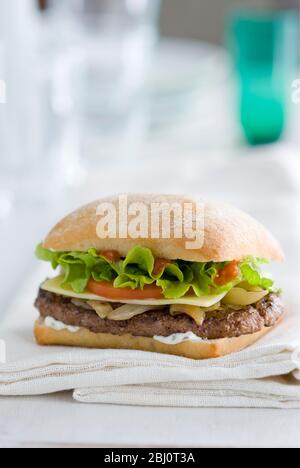 Gournet cheeseburger with salad and tomato on ciabatta bread roll on white napkin -
