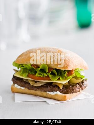 Gournet cheeseburger with salad and tomato on ciabatta bread roll on white paper napkin -
