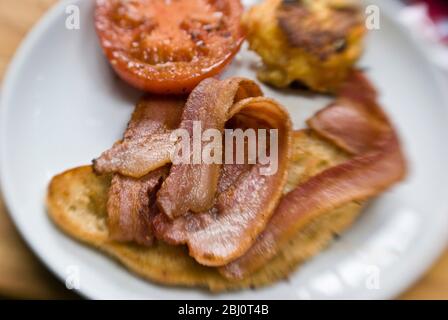 Cooked breakfast of grilled bacon, tomato, potao cake and fried bread - Stock Photo