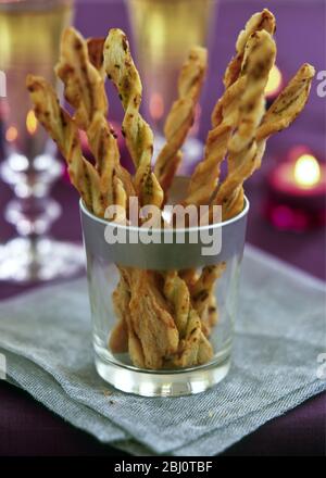 Twisted cheese straws in silver rimmed glass in candlelit party setting - Stock Photo