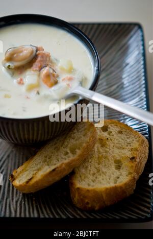 Mussel, seafood and smoked salmon chowder in pottery bowl with grilled bread - Stock Photo