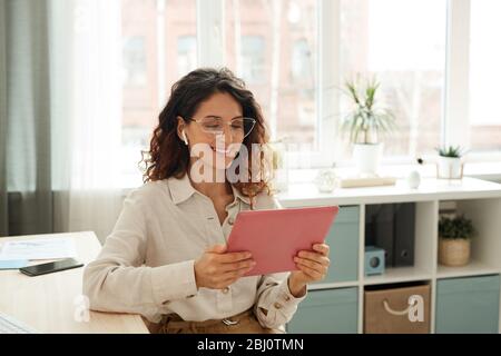 Good-looking young woman using tablet PC to participate in online meeting with her coworkers while staying at home during quarantine days Stock Photo