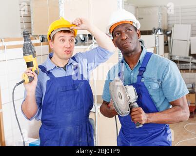 Two male contractors looking at something in surprise while working with power tools in building site indoors Stock Photo