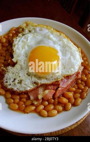 Fried egg on baked beans with streaky bacon - Stock Photo