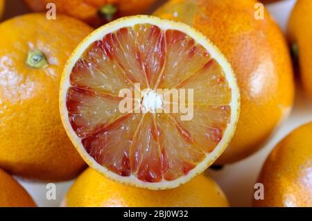 Blood orange, cut in half on white surface with whole oranges behind - Stock Photo