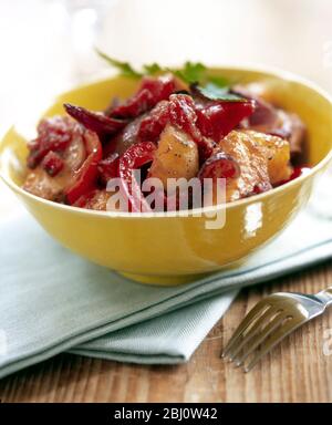 Yellow bowl of potatoes roasted with strips of red pepper and red onions with mustard dressing - Stock Photo
