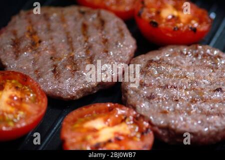 Beefburgers and halved tomatoes being grilled on non-stick grill pan -