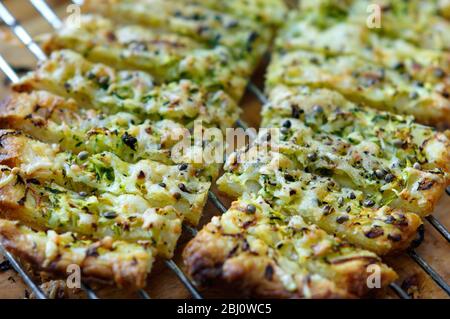 Freshly baked cheese straws cooling on rack, made with grated courgette and grated emmental strewn onto puff pastry sheet and sprinkled with hemp seed Stock Photo