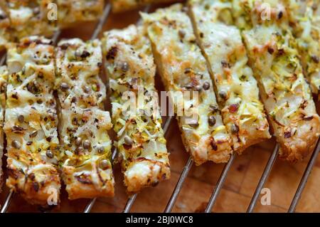 Freshly baked cheese straws cooling on rack, made with grated courgette and grated emmental strewn onto puff pastry sheet and sprinkled with hemp seed Stock Photo
