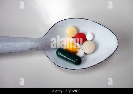 White enamel spoon of various coloured pills - Stock Photo