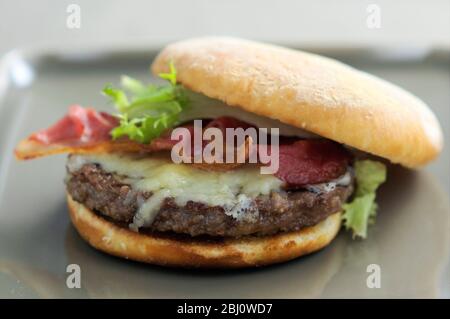 Chargrilled hamburger in bun with frisee salad, grilled bacon and melted cheese - Stock Photo