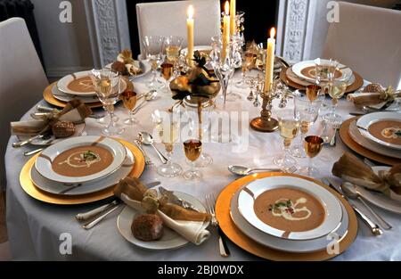 Formal festive table setting for holiday or wedding celebration with soup in large open bowls on gold edged plate on golden platters with candles and Stock Photo