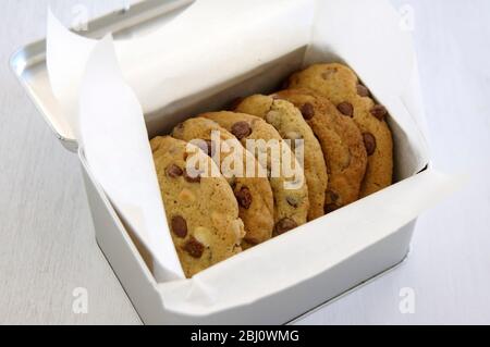 Metal tin of chocolate chip cookies wrapped in white greaseproof paper - Stock Photo