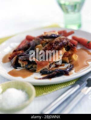 Classic British dish of Toad in the Hole, batter pudding cooked with sausages in it, served with red onion gravy and boiled carrots - Stock Photo